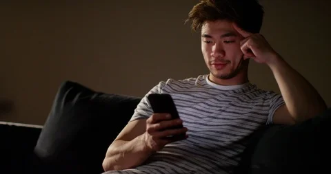 4K Young Asian man looking at phone late at night turns to smile at camera Stock Footage 86781682