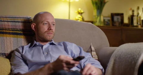 4k, Young businessman sitting on a sofa and browsing through tv channels Stock Footage 128405424