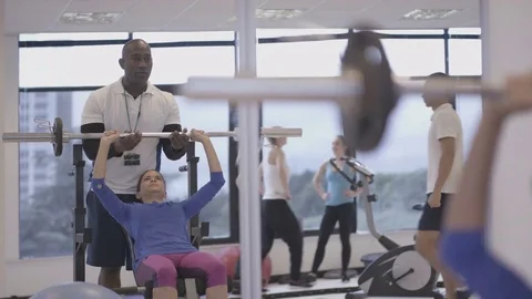 4K Young group working out in the gym, trainer spotting for girl lifting weights Video stock 75866937