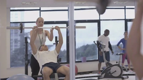 4K Young group working out in the gym, trainer spotting for guy lifting weights Video stock 75869855