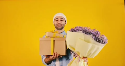 4K Young handsome man with big present box and bunch of flowers on yellow bac Stock Footage 170658121