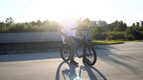 4K Young man with cap talking on the phone sitting on BMX bicycle in park Stock Footage 117724809
