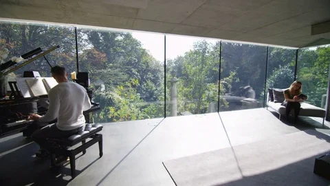 4K Young man plays the piano in contemporary home as his girlfriend listens Stock Footage