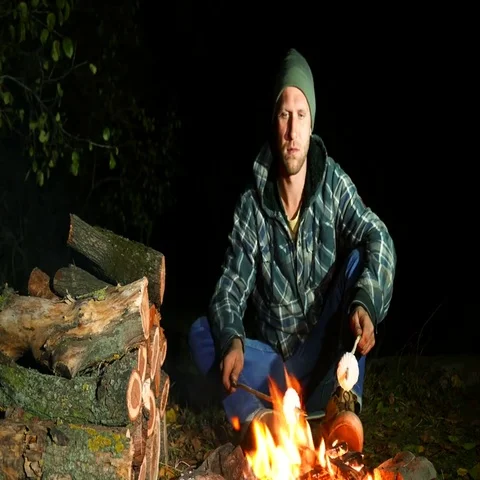 4k . young man roasting two marshmallows at camp fire Stockbeeldmateriaal 69699780