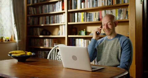 4k A young man talking on the phone while sitting with his laptop Stock Footage 128403949