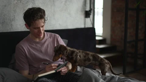 4k Young man is writing in notebook and sitting on bed with dog in bedroom spbd. Stock Footage 201255922