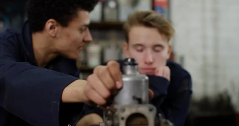 4K Young mechanic trying to teach bored apprentice in garage workshop Stock Footage 112974575