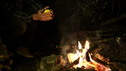  4K.Man and cup of coffee or tea in hands near  bonfire. Autumn travel life.  Stockbeeldmateriaal 70297360