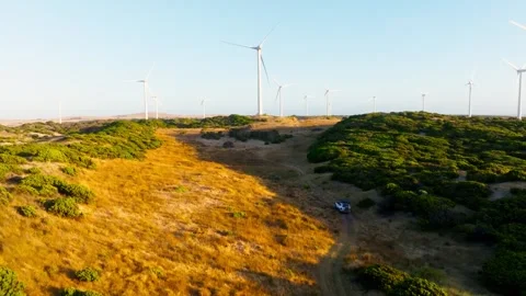 A 4x4 driving along an off-road track towards wind turbines, filmed with a drone Stock Footage 345852439