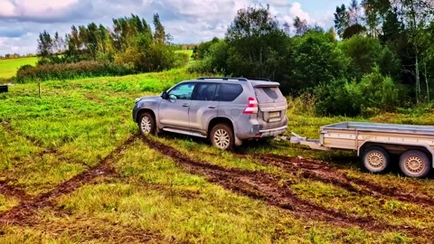 4x4 SUV towing a small utility trailer over a rugged, muddy, off-road track. Stock Footage 325685161