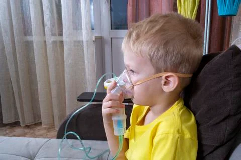 A 5-7 year old boy in a yellow t-shirt takes an inhalation at home Stock Photos