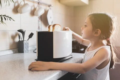 5 - 7 year old kid girl who is preparing breakfast from toast in a toaster in Stock Photos