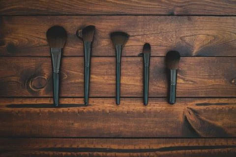5 assorted makeup brushes on a brown rustic wood background Stock Photos