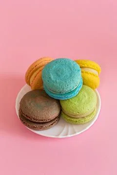 5 macaroons of different colors stacked on a small white plate on a pink tabl 스톡 사진