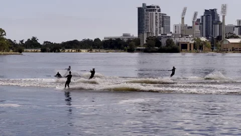 5 performance skiers speed up river past city, tree-covered bank and bridge in b Stock Footage 241981578