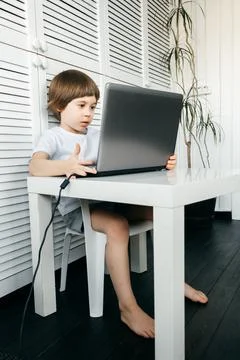 5 year boy sit at the table, uses laptop, looking at the screen. Child is doi Stock Photos