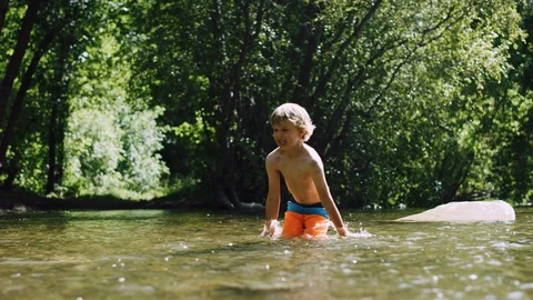 5 year old blonde boy splashes vigorously in a river on a warm summer day 8K Stock Footage 122534112