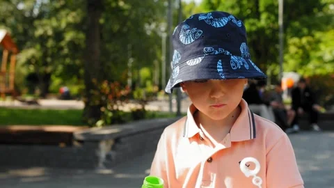 A 5 year old boy in a blue bucket hat creates soap bubbles to music on the Stock Footage 279064450