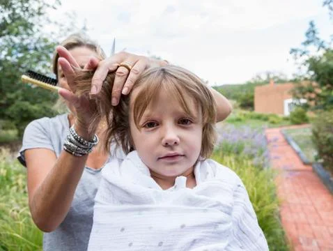 5 year old boy getting his hair cut by mother outside Stock Photos