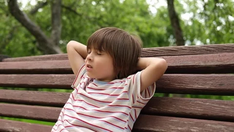 A 5-year-old boy is resting on a park bench with his hands behind his head. Stock Footage 312515594