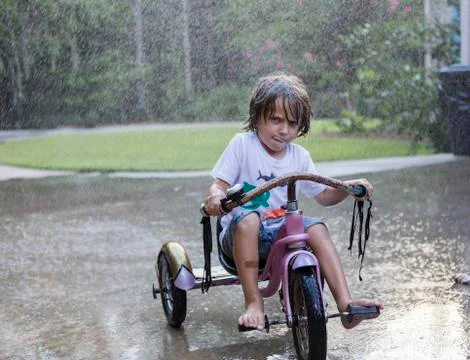 5 year old boy riding his tricycle bike in the rain Stock Photos