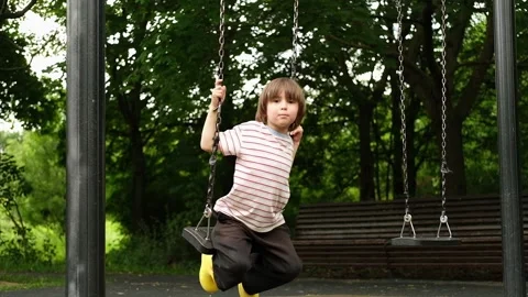 A 5 year old boy is swinging on a swing in the park. A child is playing on an Stock Footage 312515627