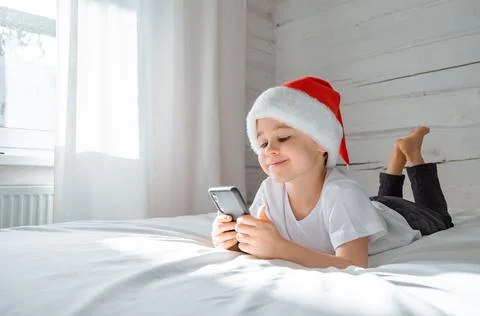 5 year smiling boy is lying on bed looking at the screen and playing smartpho Stock Photos