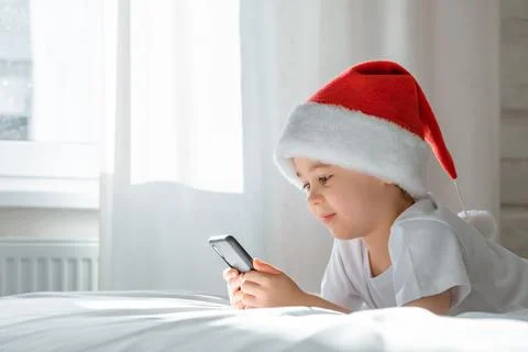 5 year smiling boy is lying on bed looking at the screen and playing smartpho Stock Photos