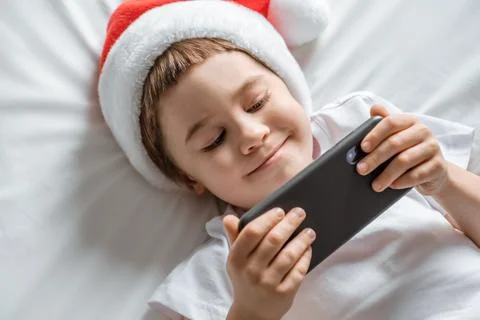 5 year smiling boy is lying on bed looking at the screen and playing smartpho Stock Photos