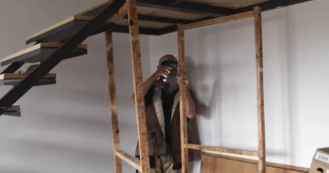 50 year old man assembling wooden shelf at home using battery powered drill Stock Footage 321880627