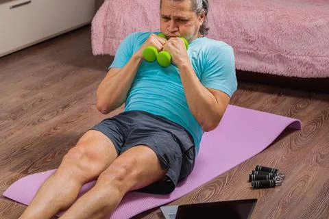 50 year old man performs exercises lying on mat at home looking at computer Stock Photos