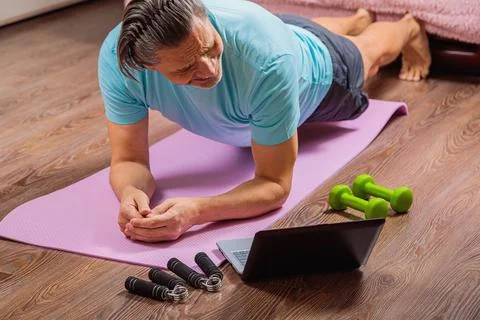 50 year old man performs exercises lying on mat at home looking at computer Stock Photos