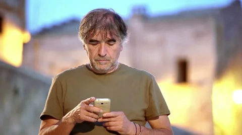 50 year old man writes a message with his smartphone in the ancient city Stock Footage