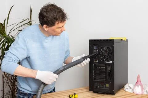 A 53-year-old man cleans dust from a computer system unit with a vacuum cle.. Stock Photos