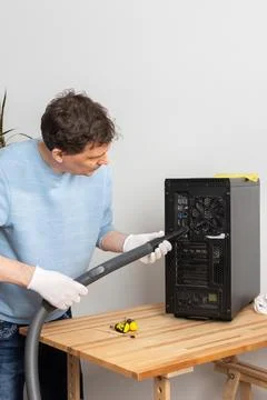 A 53-year-old man cleans dust from a computer system unit with a vacuum clean Stock Photos