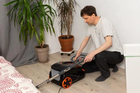 A 53-year-old man is getting ready to clean the floor with a vacuum cleaner.. Foto stock
