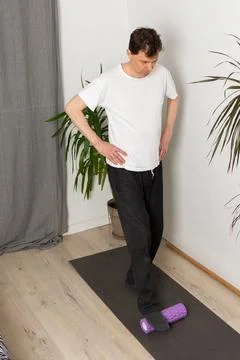 A 53-year-old man is performing exercises at home. He stands on a mat with .. Stock Photos