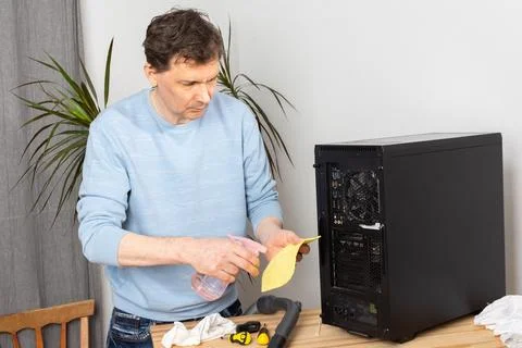 A 53-year-old man removes dust from a computer system unit while standing at  Stock Photos