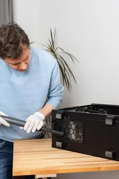A 53-year-old man uses a vacuum to clean dust from a computer system unit on  Stock Photos