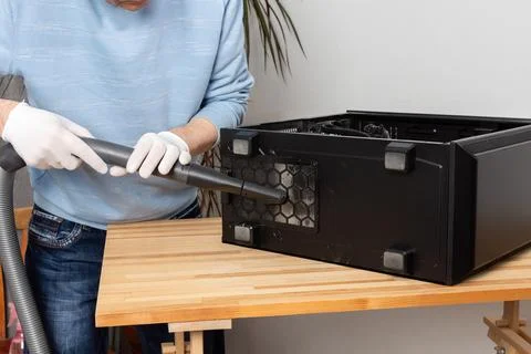 A 53-year-old man uses a vacuum to clean dust from a computer system unit on  库存照片