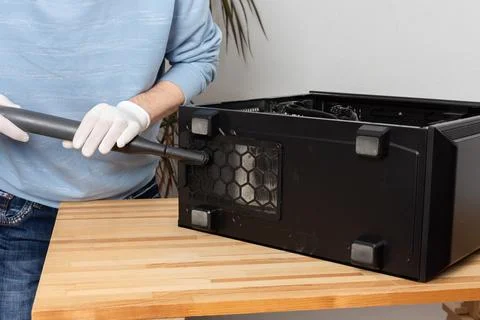 A 53-year-old man uses a vacuum to clean dust from a computer system unit on  Stock Photos