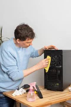 A 53-year-old man uses a cloth to clean dust from a computer system unit. He  Stock Photos