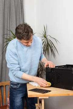 A 53-year-old man uses a cloth to clean dust from a computer system unit. H.. Stock Photos