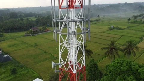 5g telecom tower close up drone aerial revealing green rice field plowed land Video stock 143636228