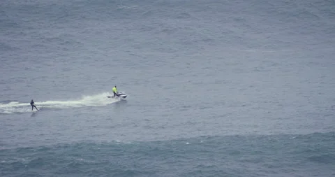 5K Distant view of pro surfer wakesurfing behind jet ski driver in blue ocean Stock Footage 157715642