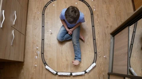 A 6-7 year old boy is playing alone with a children's railroad Stock Footage 198383039
