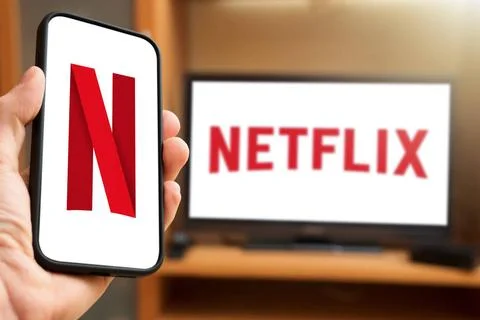  6 April 2024: Man holding smartphone with Netflix logo in front of a TV s... Foto stock