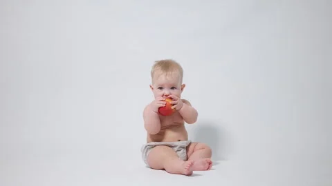 A 6-month-old baby eats a red apple, video shot against a light background Stock Footage 242779520