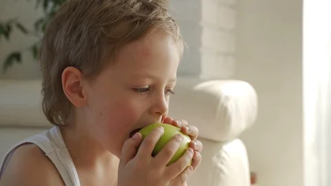 6 year old boy eating green apple and try pull out baby teeth Stockbeeldmateriaal 107922376