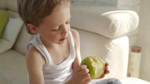 6 year old boy eating green apple and try pull out baby teeth Stock Footage 107929948